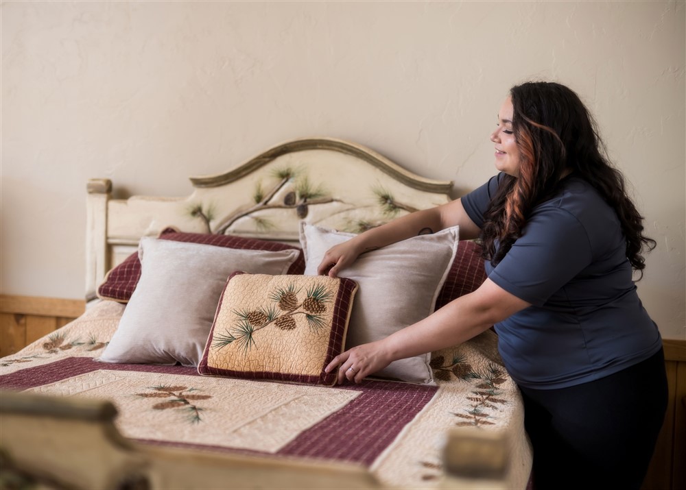 A cleaner adjusts the cushion on a freshly made bed inside a bedroom. 